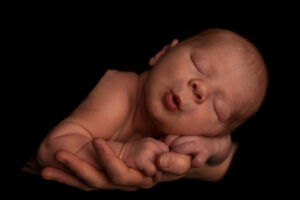 Newbornfotos von Baby auf der Hand von Papa mit schwarem Hintergrund