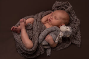 Schlafender Newborn-Junge mit Plüschtier im Arm